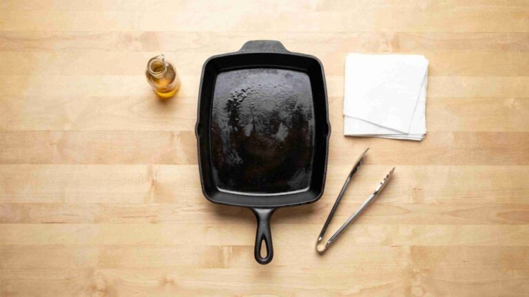 Cast iron griddle pan with oil, paper towels, and tongs laid out to season a griddle pan.