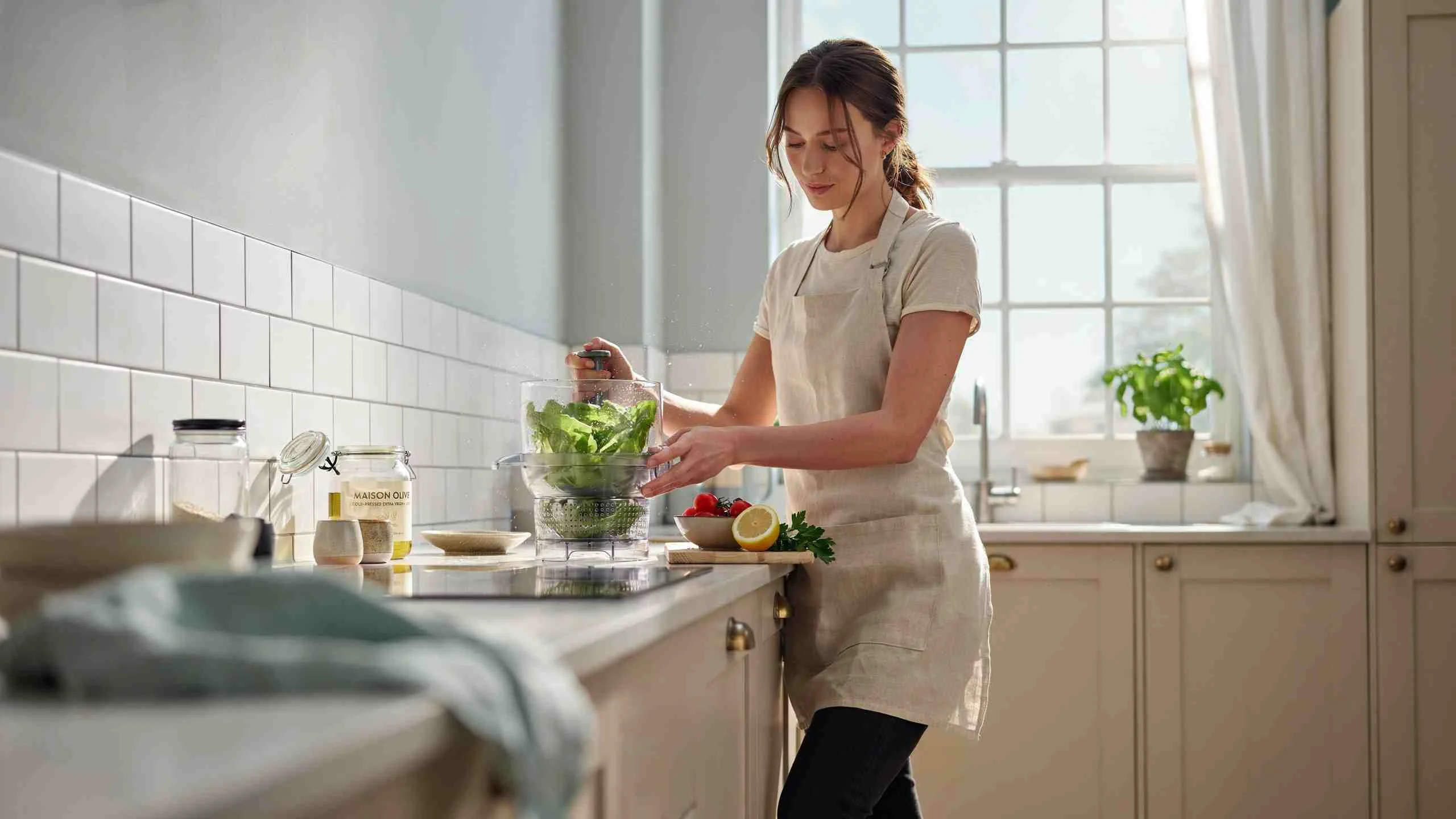 Woman showing how to dry lettuce with salad spinner in a modern kitchen while preparing fresh salad.
