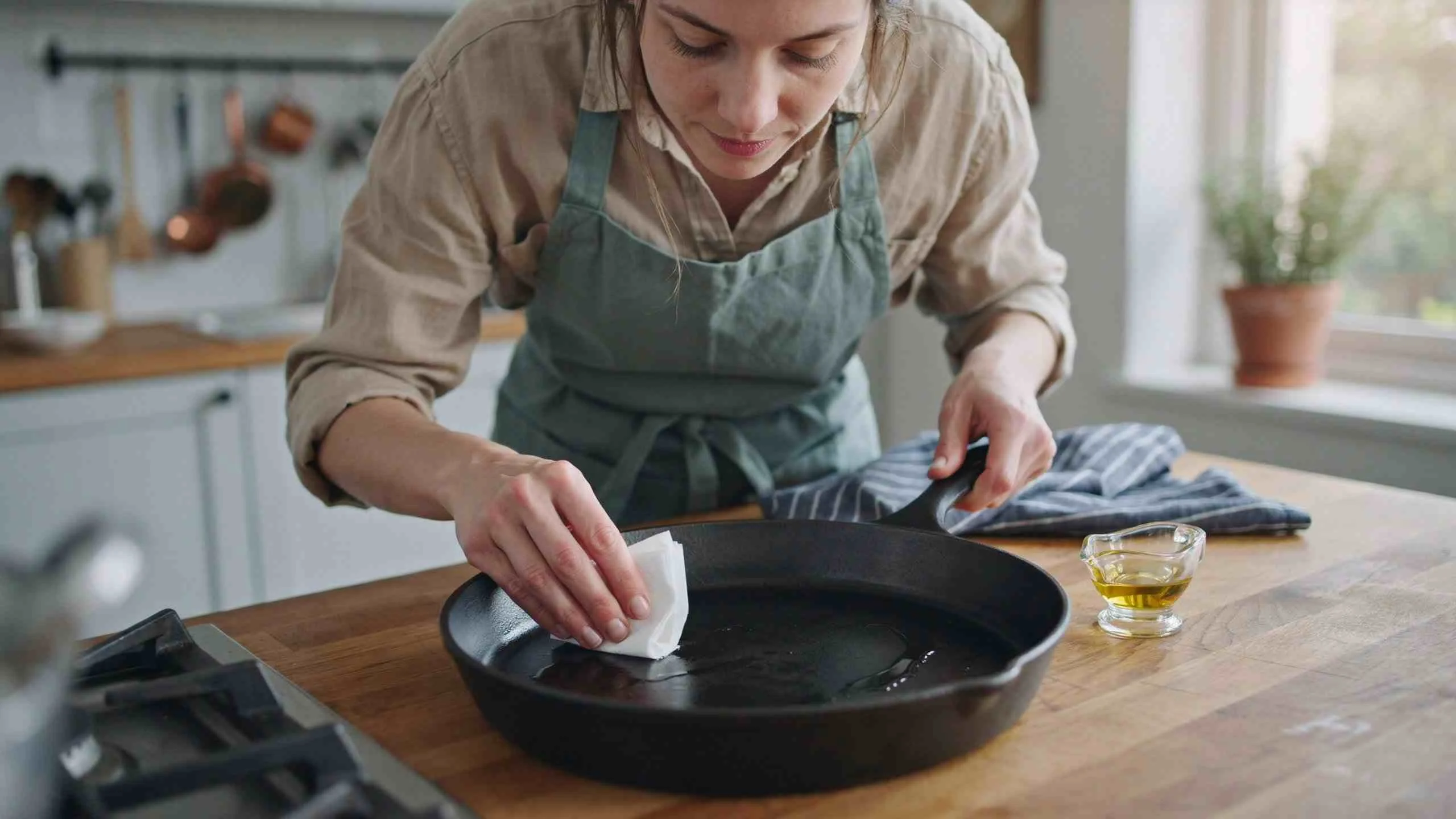 Woman seasoning a cast iron griddle pan with a thin layer of oil in her home kitchen.